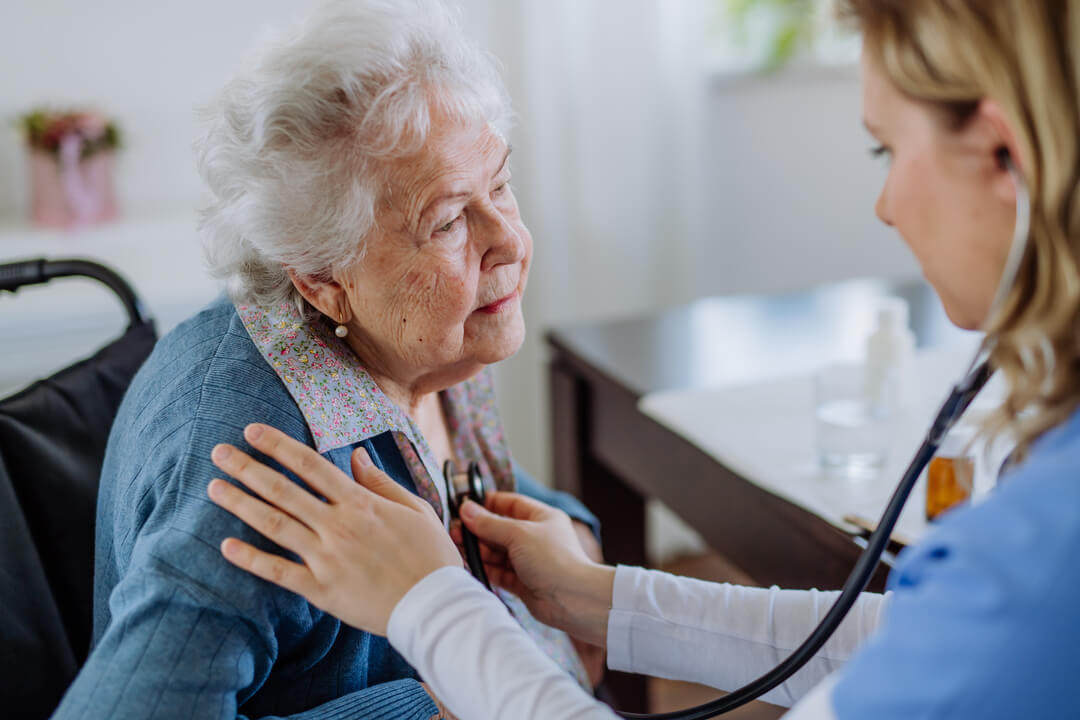 Nurse examining senior patient with stethoscope at her home.